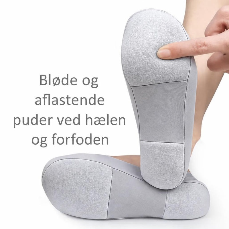 Grå lave strømper med polstrede såler, hvor en finger trykker på forfoden