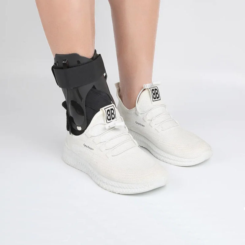 Sort stabiliserende ankelstøtte med skinner og justerbar rem over hvid sneaker