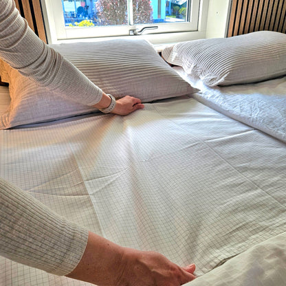 Hænder retter et hvidt jordingslagen med fine tern på sengen