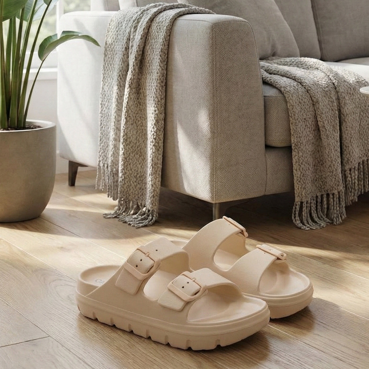 Beige dametøfler med to spænder på trægulv ved sofa