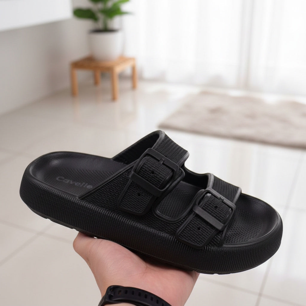 Sort justerbar cloud-toffel med to spænder holdt i hånden